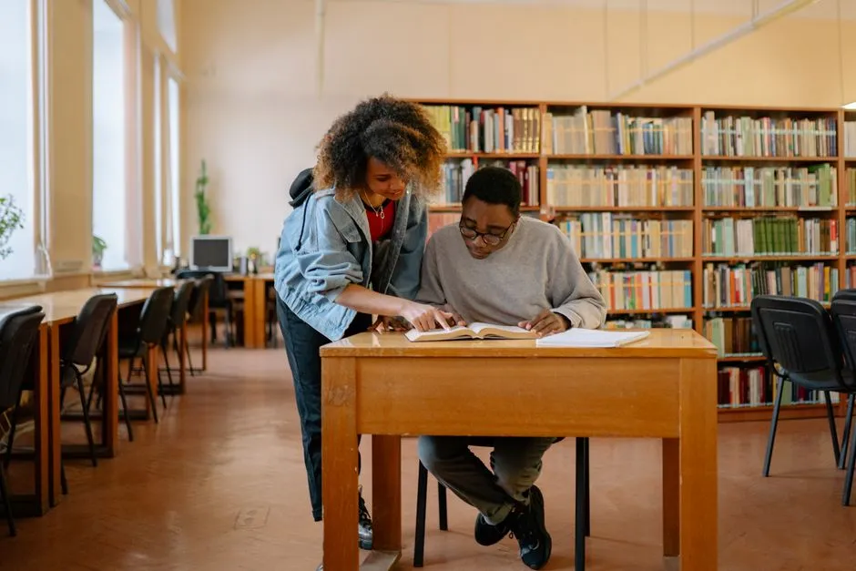 Two students at a library desk comparing puzzle results on their phones